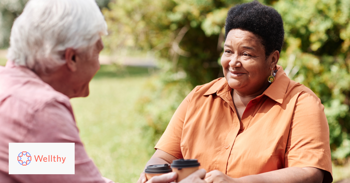 A caregiver is having a cup of coffee with a care recipient outside on a picnic table