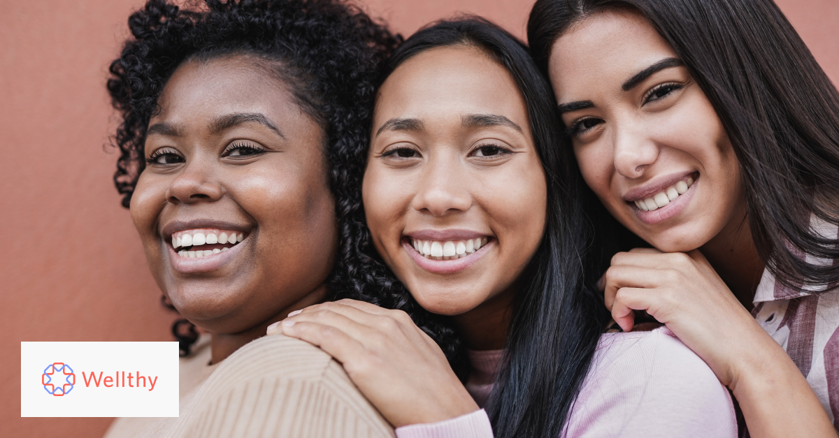 Three women of color smiling and hugging each other's shoulders.