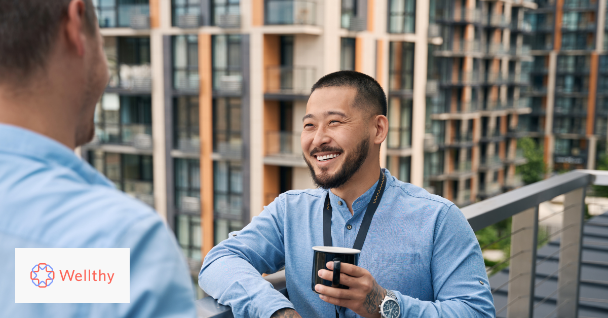 Two male coworkers on a balcony taking a coffee break and laughing.