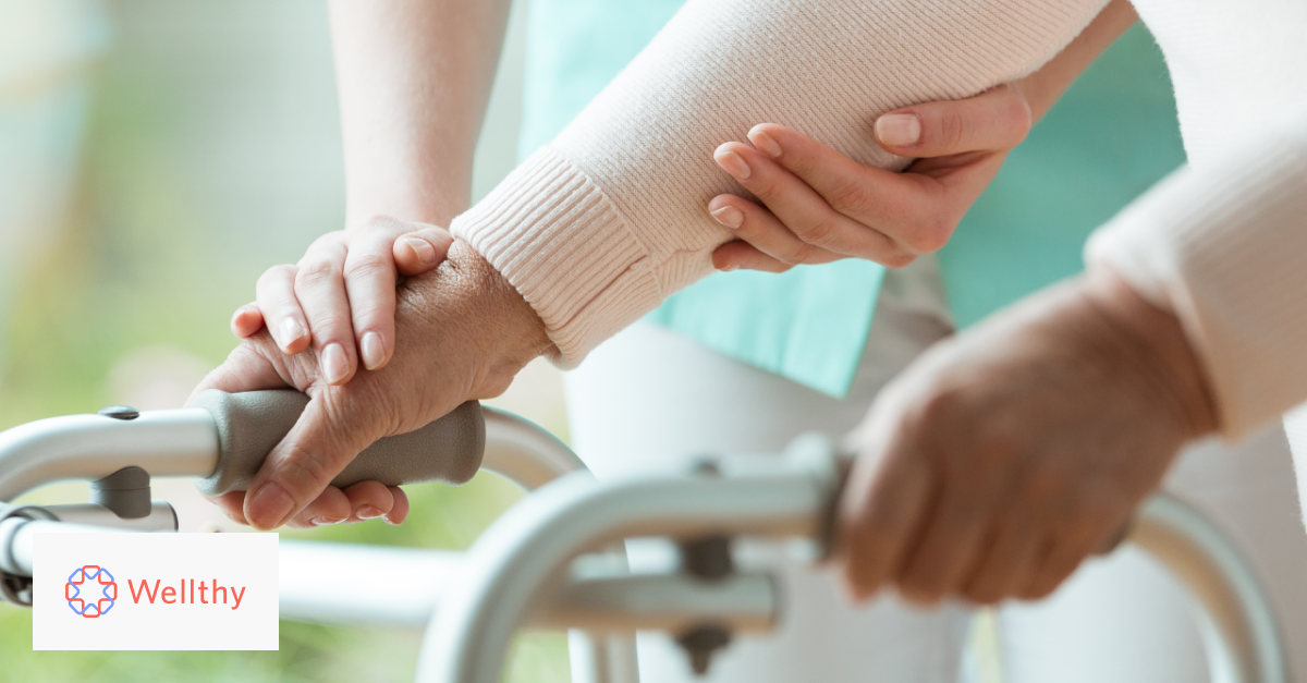 A close-up photo showing an elderly person leaning on their worker with their caregiver gently holding their right hand and arm.