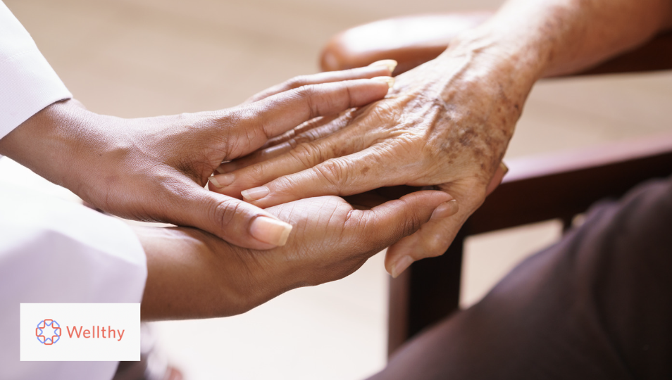A photo of a woman holding an elderly woman's hand in a hospice setting.