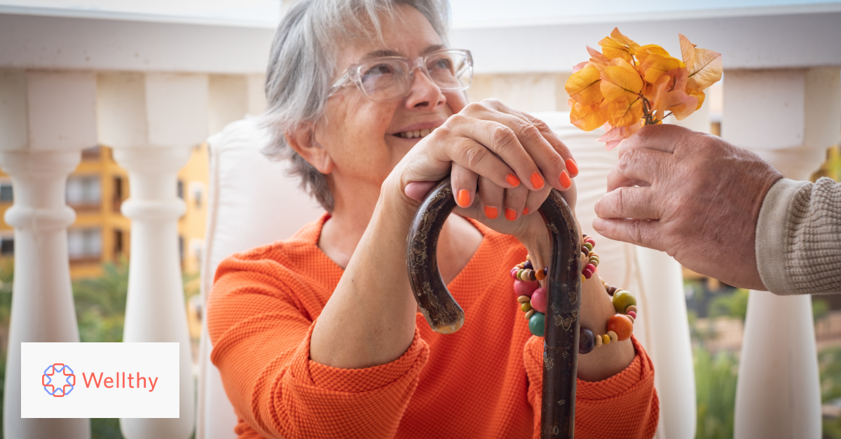 An older woman holding a cane smiles as her caregiver hands her a bouqet of flowers. 